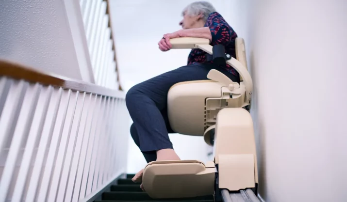 Senior Woman Sitting On Stair Lift At Home To Help Mobility